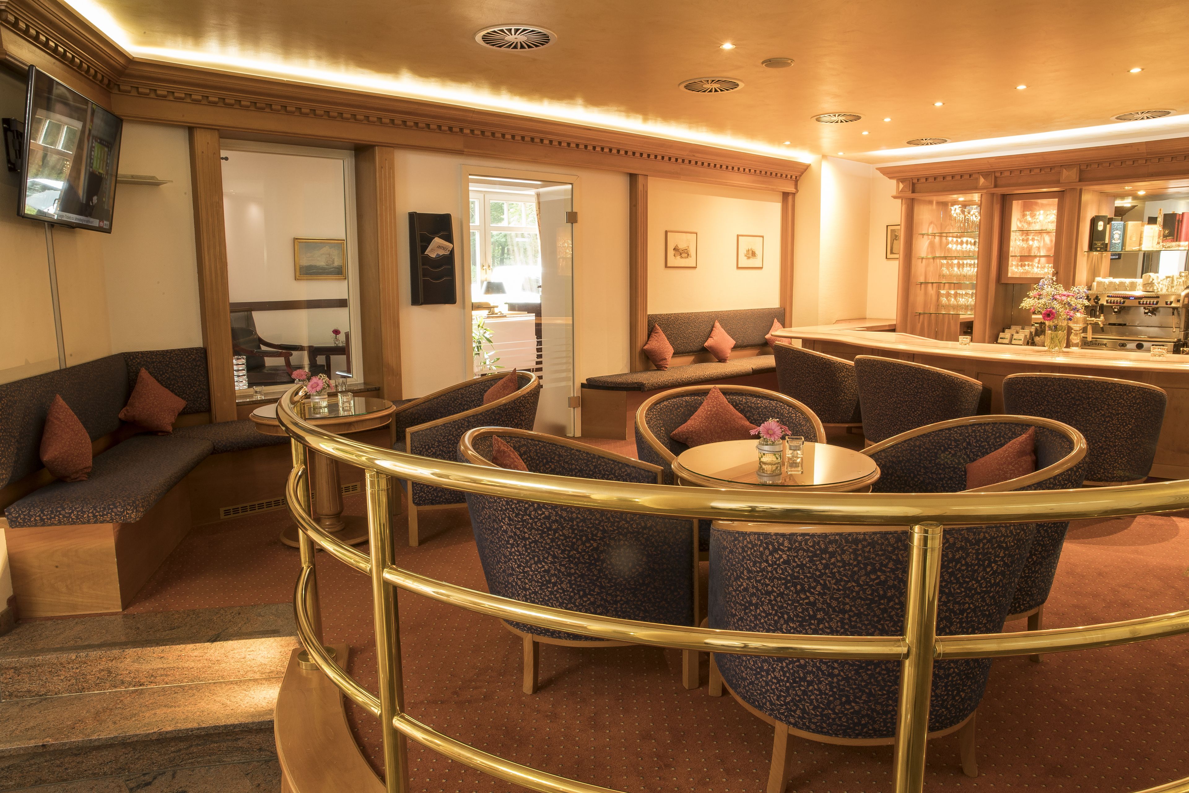Una hall d'albergo con una zona salotto a forma di curva, un bar e un televisore a parete.