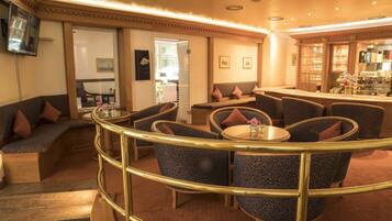 Una hall d'albergo con una zona salotto a forma di curva, un bar e un televisore a parete.