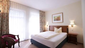 Quarto de hotel com uma cama, uma cadeira, uma mesinha de cabeceira e uma luminária na parede.