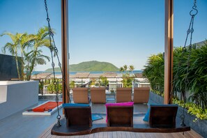 A balcony with wicker chairs, a swing, and a view of the sea and hills. - Almali Luxury Residence (Rawai)