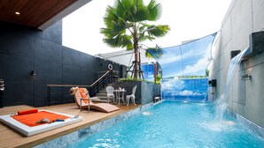 A modern indoor pool with a wooden deck, lounge chairs, and a palm tree. - Almali Luxury Residence (Rawai)