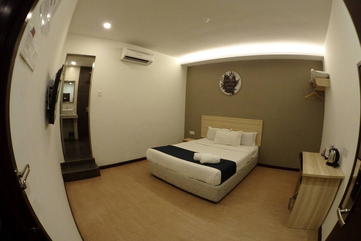 Una habitación de hotel con cama, mesita de noche y aire acondicionado instalado en la pared.