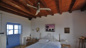 Une chambre à coucher avec un lit, un ventilateur de plafond, une porte bleue, un bureau et une chaise.