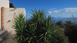 Un bâtiment à l’extérieur blanc, avec un tuyau rouge, et une vue sur la mer et les montagnes en arrière-plan.