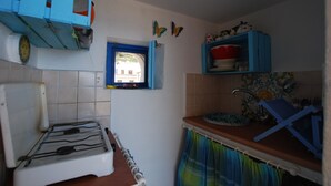 Une cuisine de taille réduite, équipée d’une cuisinière à gaz, d’une petite fenêtre et de meubles de couleur bleue.