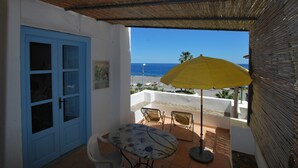 Un balcon avec une table et des chaises, un parasol jaune et une vue sur la mer.