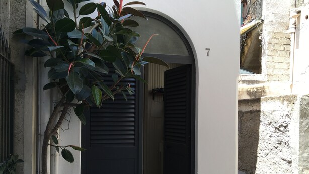 A narrow street with a building featuring a black shuttered door and a small entrance. - Capperino Mono (Lipari)