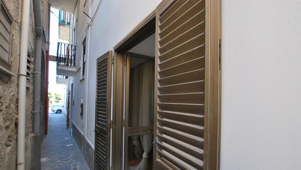 A narrow alleyway with a stone floor, a metal grate, and a wooden door with shutters. - Pomice Studio (Lipari)