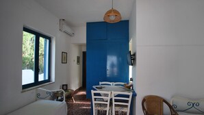 A room with a bed, a table with chairs, a wicker chair, a window with blue trim, and a blue door. - Villino Vulcano (Lipari)