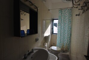 A bathroom with a bathtub, toilet, and a window with a curtain. - Villino Vulcano (Lipari)