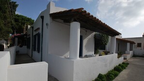 A white building with a tiled roof, a concrete pathway, and a small garden area. - Villino Vulcano (Lipari)