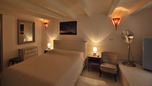 A bedroom with a large bed, bedside tables with lamps, a chair, a floor fan, a mirror, and a wall-mounted picture. - Discesa Delle Capre (Palermo)