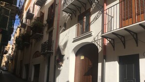 A narrow street with buildings featuring balconies and wooden doors. - Discesa Delle Capre (Palermo)
