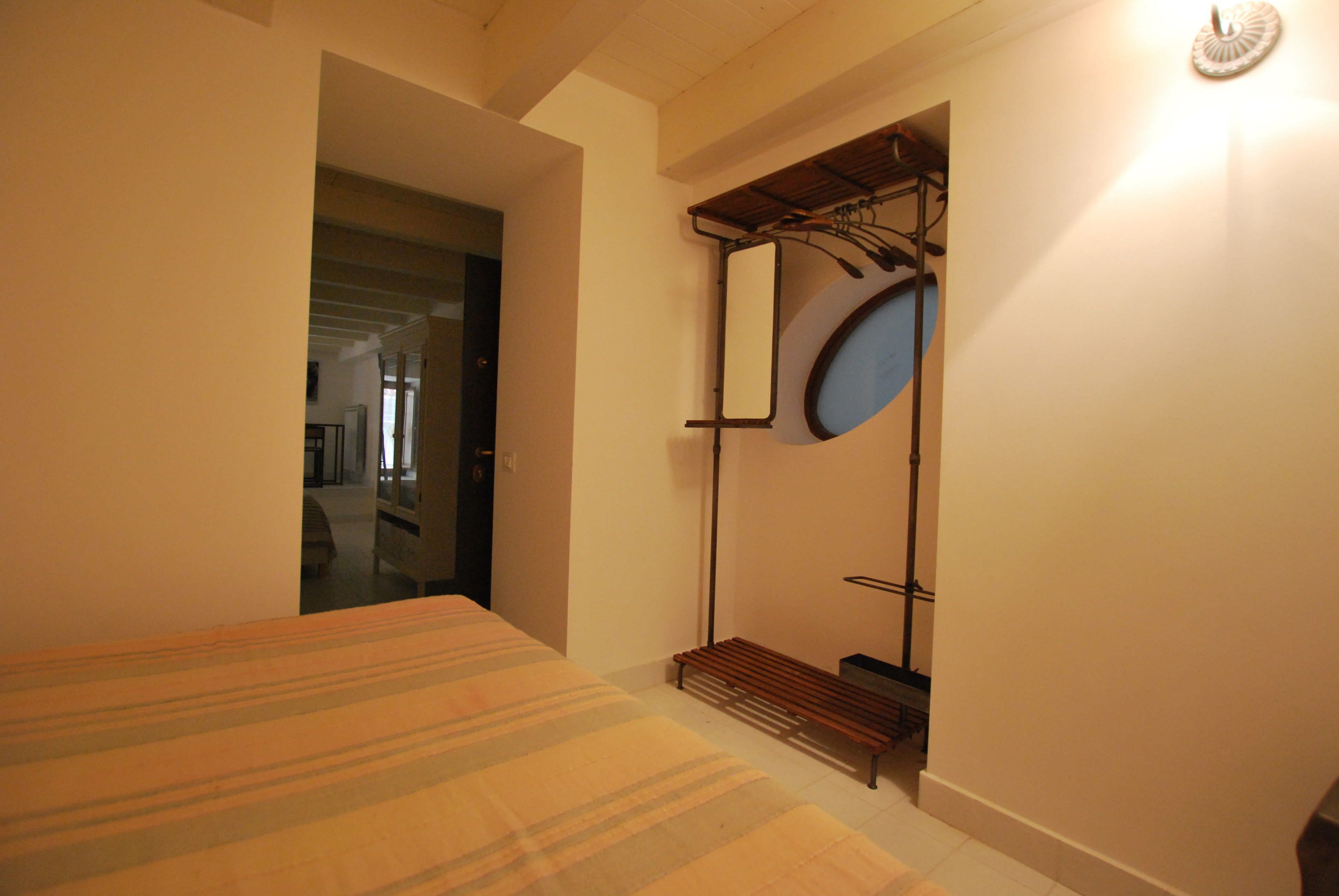 A bedroom with a bed, a bench, a mirror, and a coat rack.