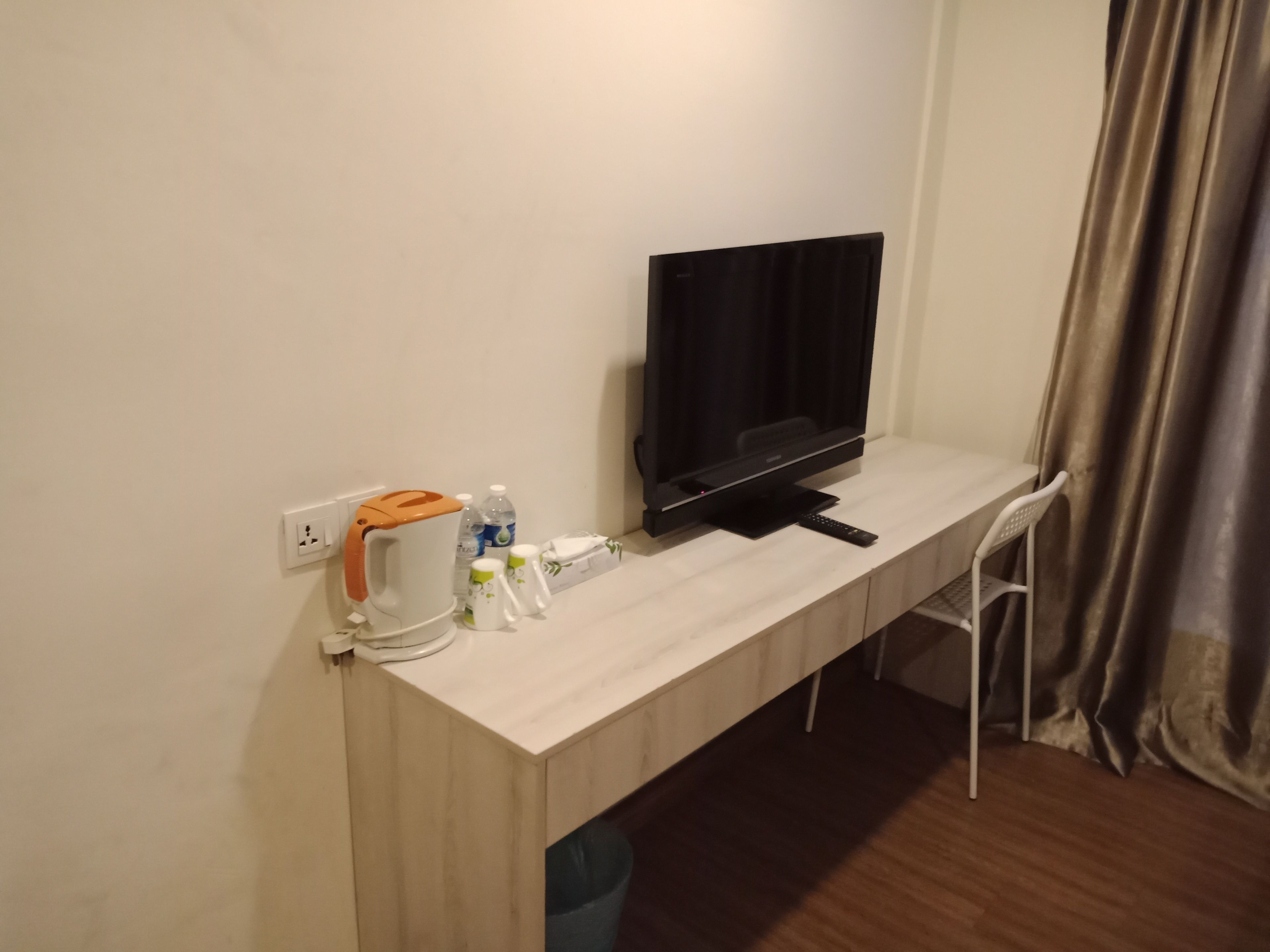 Et hotelværelse med et træskrivebord, et fladskærms-tv, en elkedel og en stol.