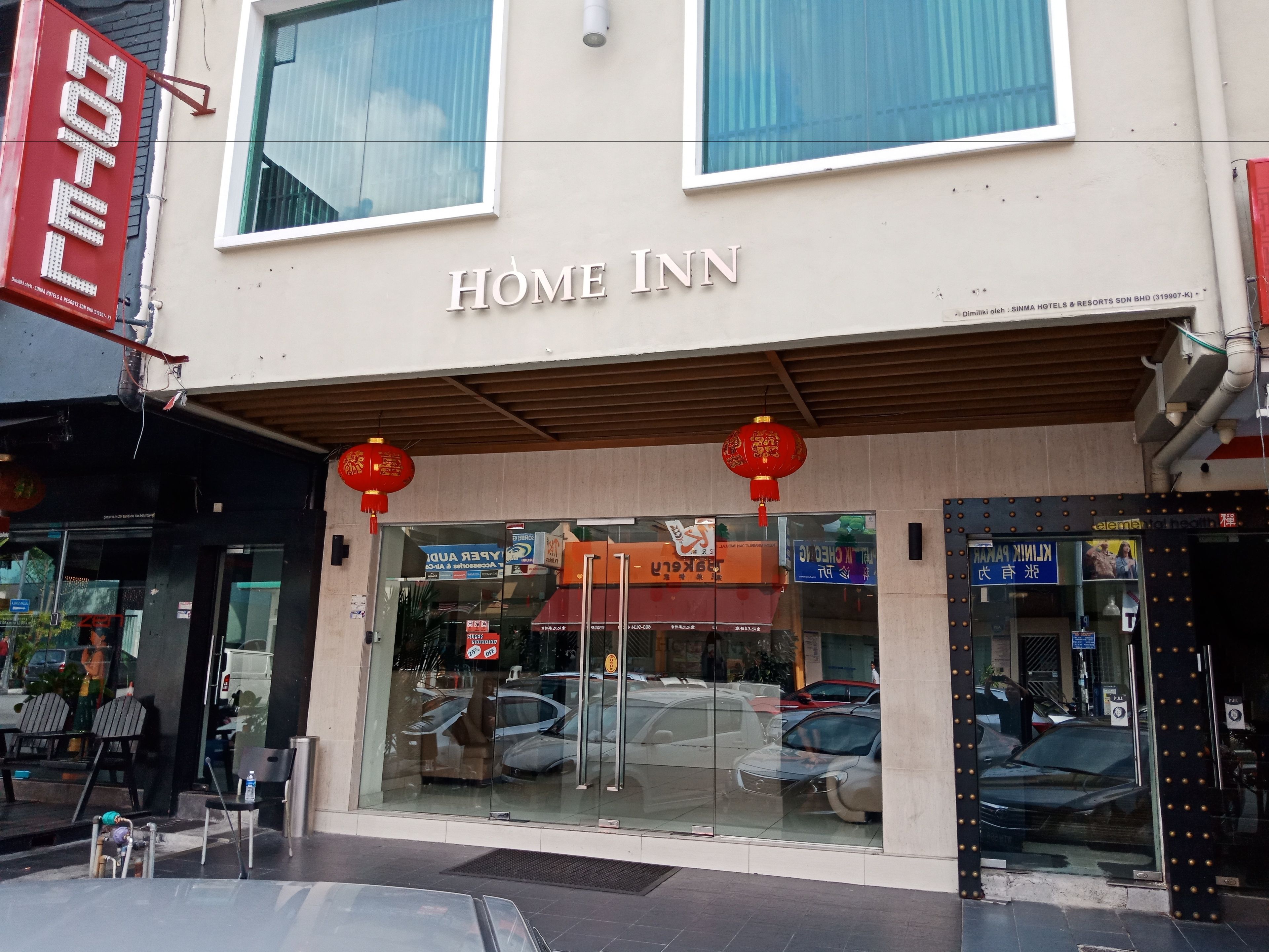 A hotel named "Home Inn" with a modern facade, large windows, and a visible car parking area in front.