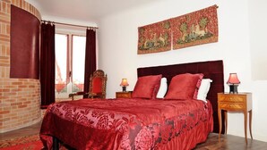 A room with a large bed, a red carpet, a wooden nightstand, and a tapestry on the wall. - Hôtel la Tour (Sully-sur-Loire)