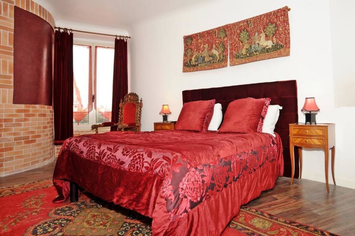 A room with a large bed, a red carpet, a wooden nightstand, and a tapestry on the wall.
