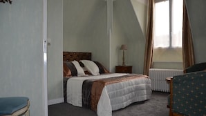 A bedroom with a bed, a chair, a nightstand, and a window with curtains. - Hôtel la Tour (Sully-sur-Loire)
