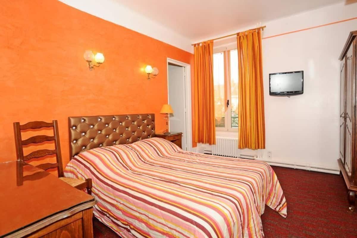 A hotel room with a bed, a desk, a chair, a television, and a window with curtains.