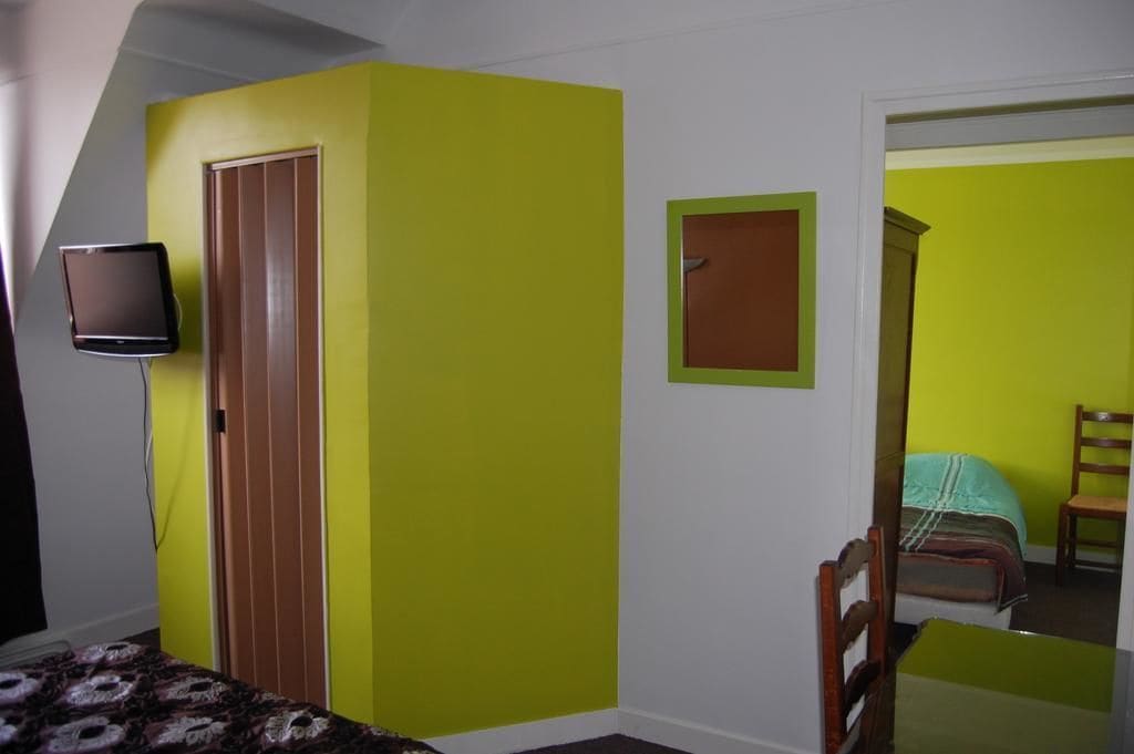 Une pièce comprenant un lit, une chaise, un téléviseur fixé au mur et une porte.