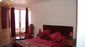 A bedroom with a large bed, a wooden nightstand, a chair, a small table, and a window with curtains.
