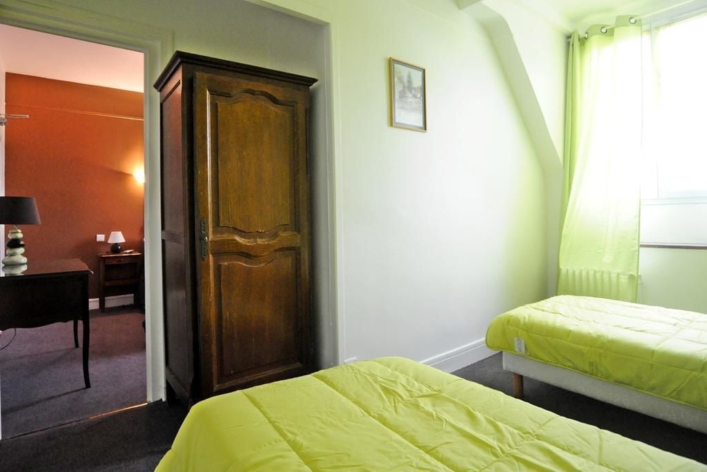 Une chambre avec deux lits, une armoire en bois, un bureau avec une lampe et un tableau encadré au mur.