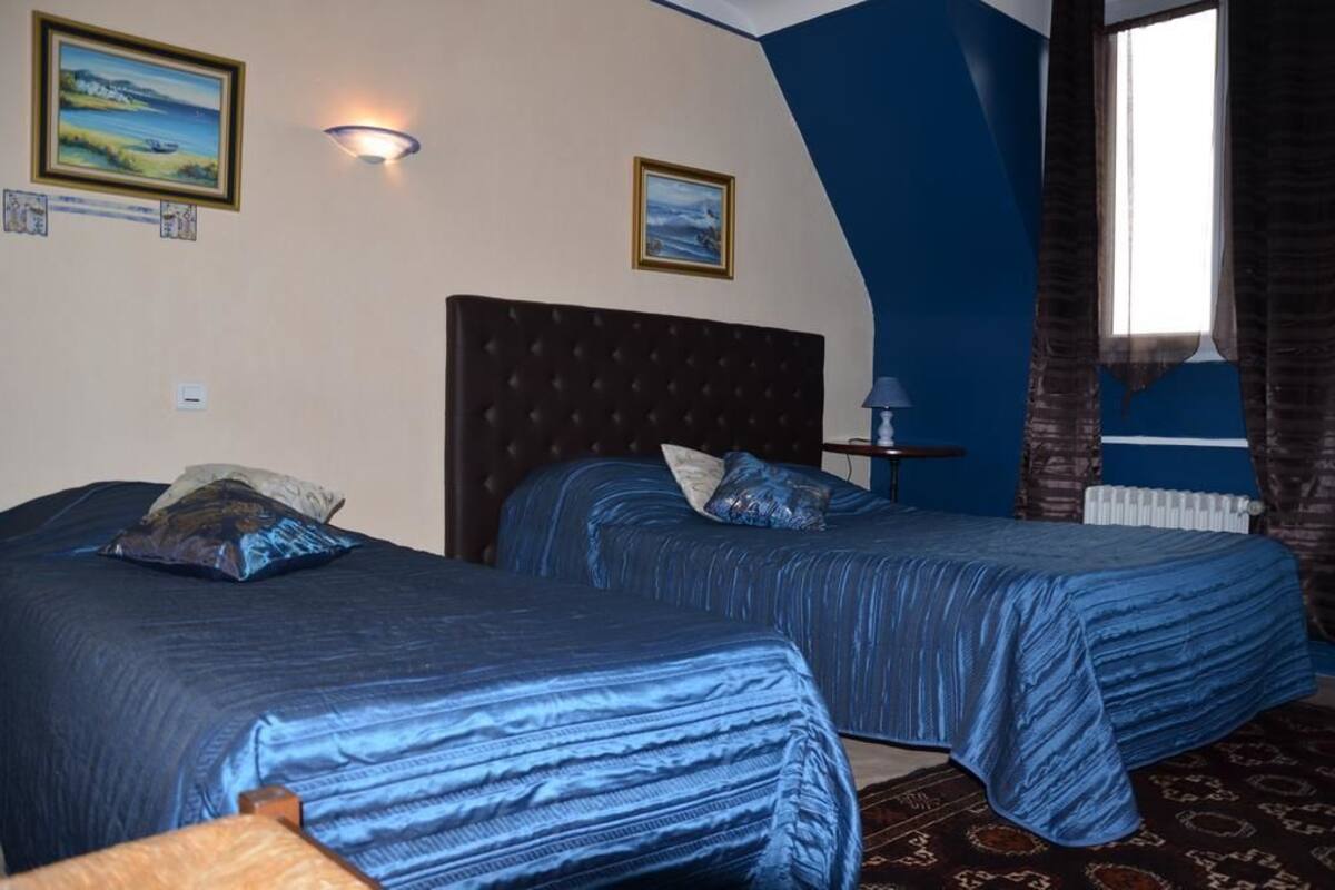 A hotel room with two beds, a nightstand, a lamp, and a window with curtains.