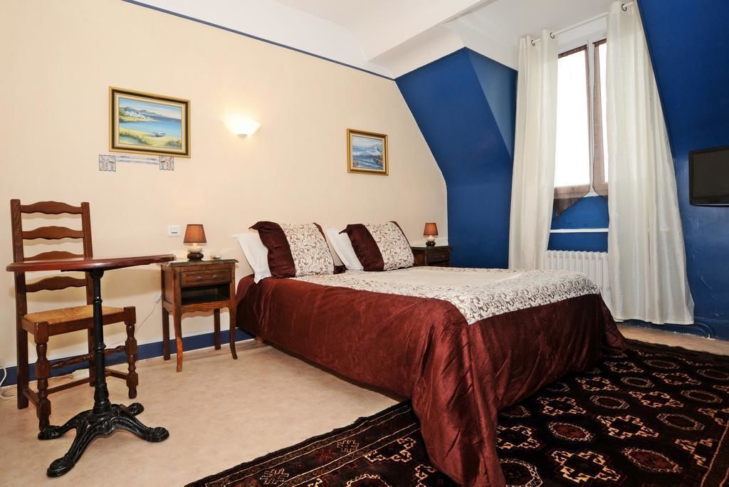 Un dormitorio con una cama, una silla, una mesa y dos cuadros en la pared.