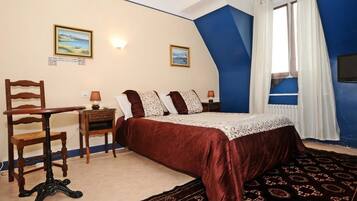 Un dormitorio con una cama, una silla, una mesa y dos cuadros en la pared.