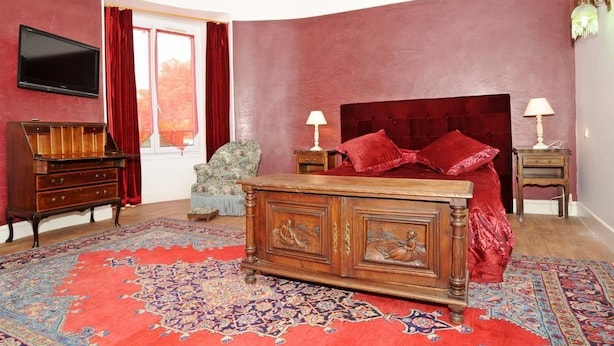 A bedroom with a large bed, two bedside tables, a TV mounted on the wall, a wooden dresser, and a patterned rug. - Hôtel la Tour (Sully-sur-Loire)