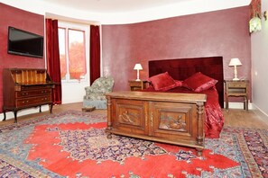Une chambre avec un grand lit, deux tables de chevet, un téléviseur fixé au mur, une commode en bois et un tapis à motifs.