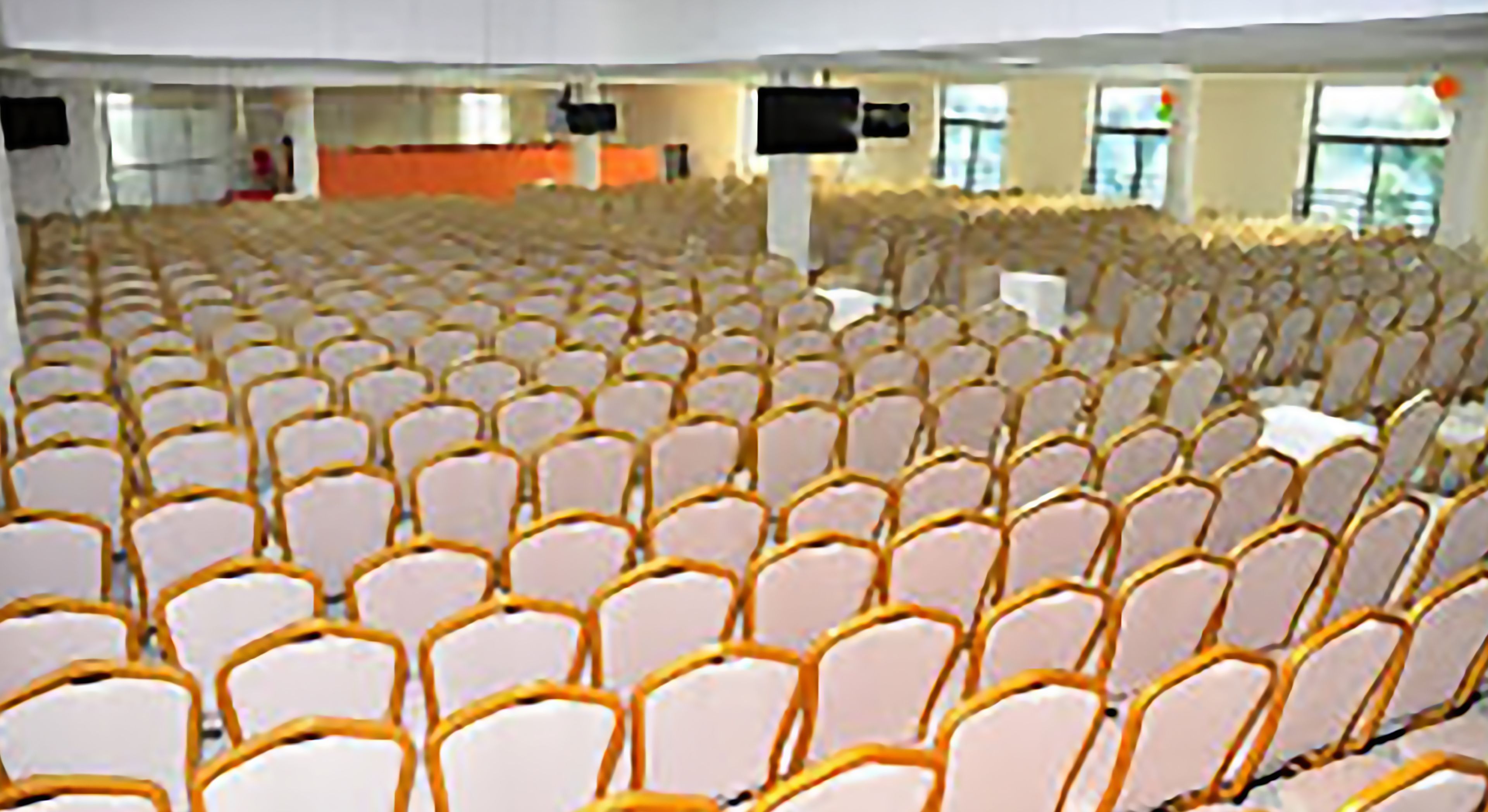 A large indoor space with rows of white chairs and orange armrests, likely a conference or event hall.