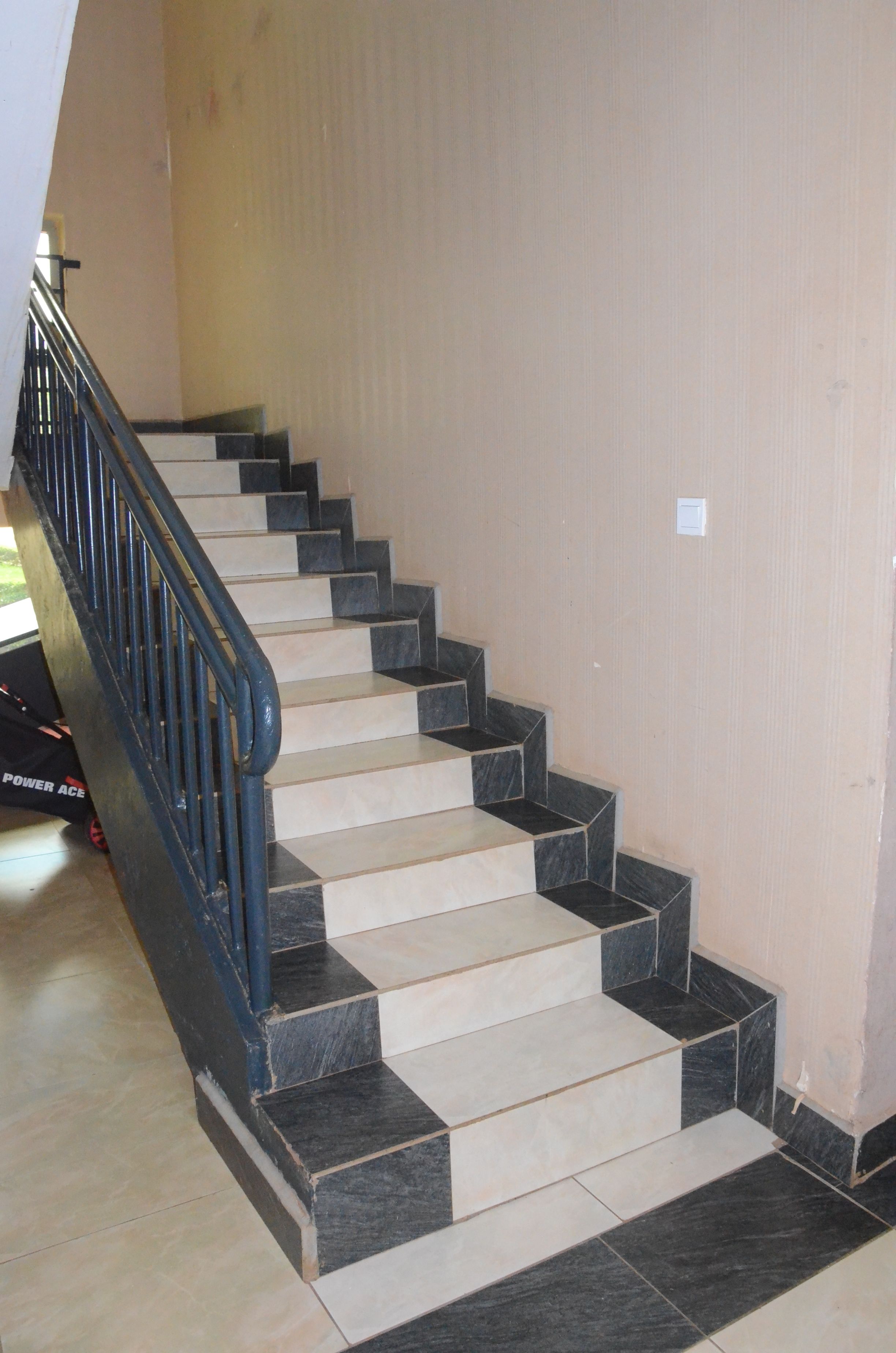 A staircase with alternating black and beige tiles, a black handrail, and a beige wall.