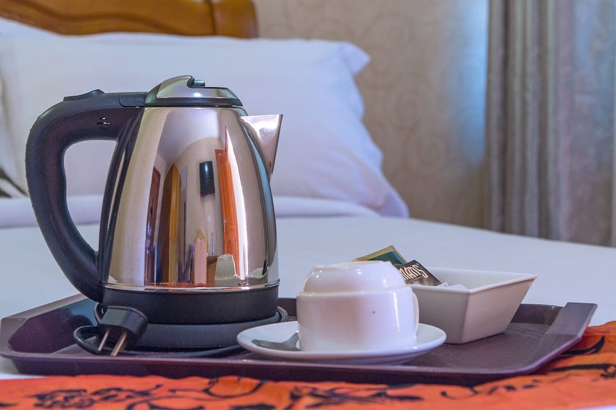 A hotel room with a bed, a bedside table with a kettle, a cup, and a tray with tea bags.