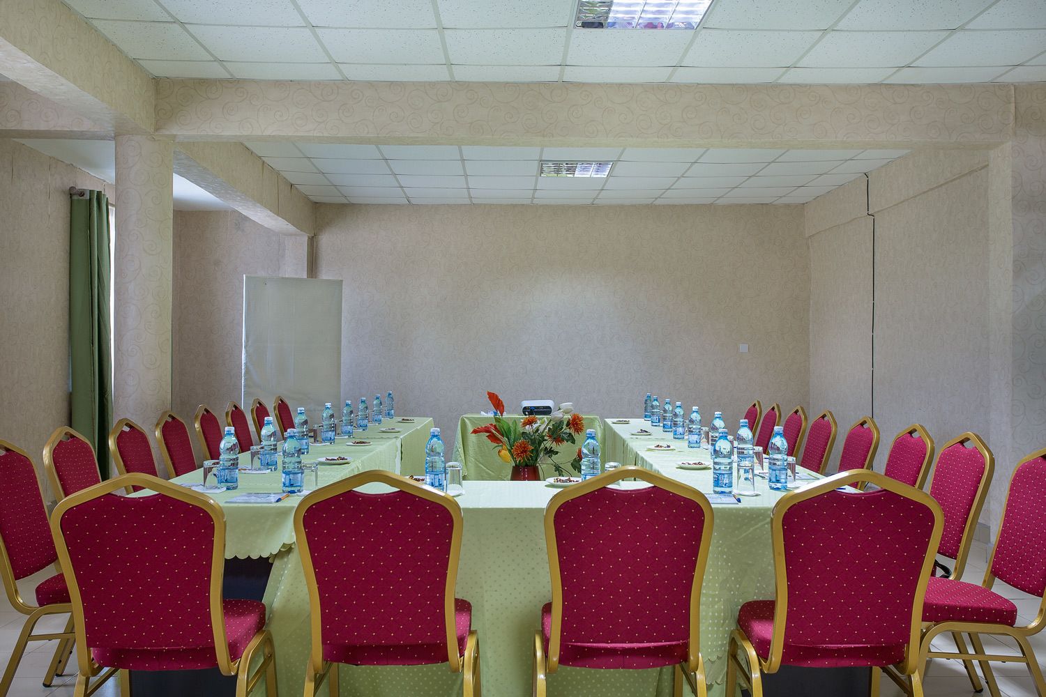 Une salle de conférence avec une longue table, des chaises rouges et des bouteilles d’eau.