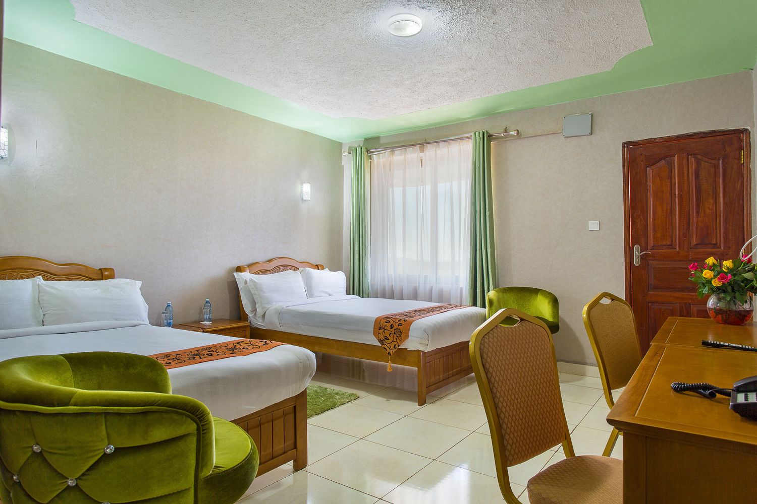 Habitación de hotel con dos camas, una mesa de comedor, sillas, una puerta de madera y una ventana con cortinas.