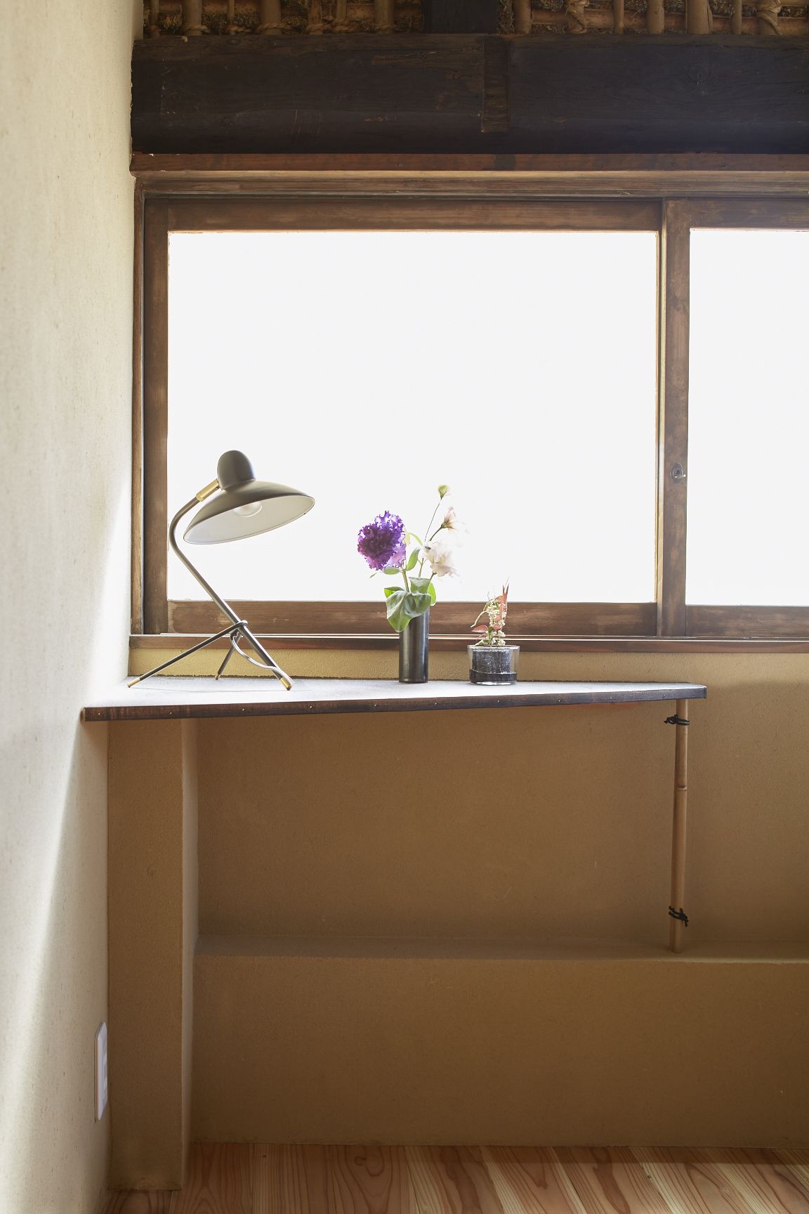 Una ventana con un escritorio, una lámpara y un florero con flores.
