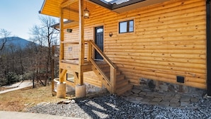 A wooden cabin with a balcony, stone steps, and a view of the surrounding forest. - Peaceful Cabin with mountain view! Hot tub, fire-pit and indoor fireplace! (Fairview)
