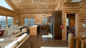 A spacious cabin with a wooden interior, a kitchen area, and a cozy living room with a sofa and a fireplace. - Peaceful Cabin with mountain view! Hot tub, fire-pit and indoor fireplace! (Fairview)