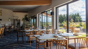 Un restaurante con mesas y sillas de madera, grandes ventanales y vistas al exterior.