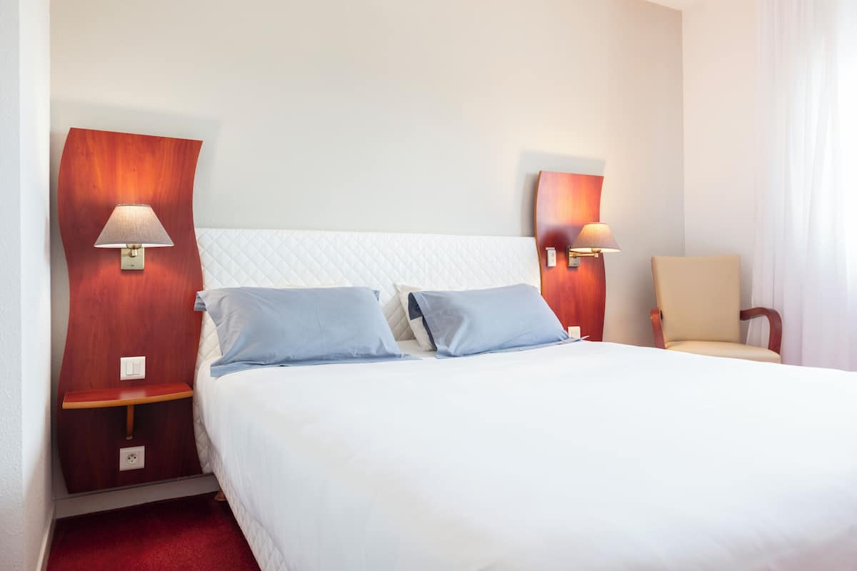 A hotel room with a large bed, two bedside tables, two wall-mounted lamps, and a chair.