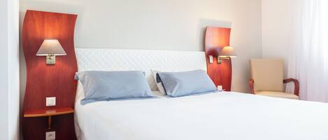 A hotel room with a large bed, two bedside tables, two wall-mounted lamps, and a chair.
