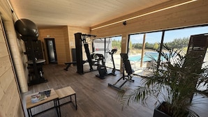 Un gimnasio con equipo de ejercicio, una banca y un ventanal con vistas a una piscina.