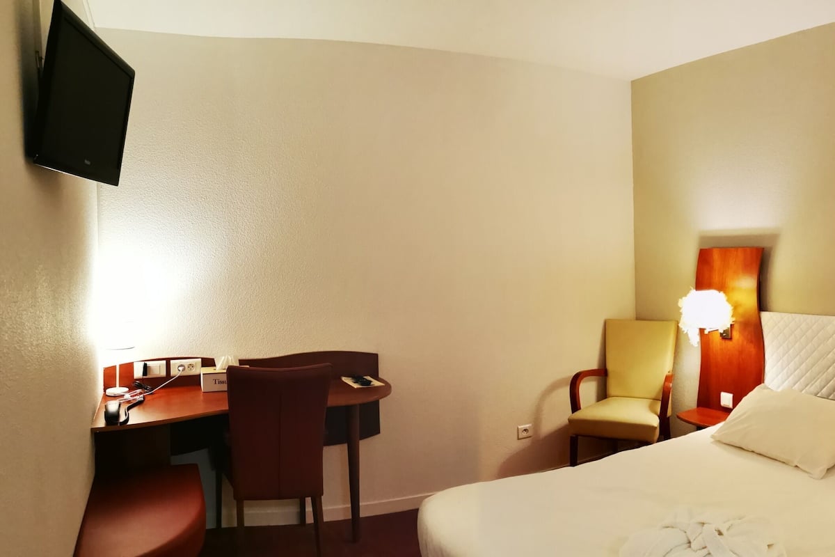 A hotel room with a bed, bedside tables, a desk, chairs, and a TV.