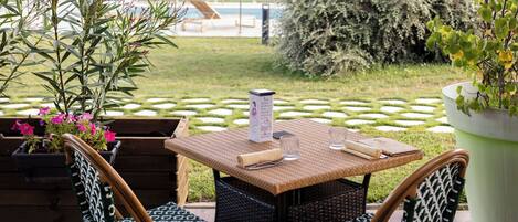 Un espace extérieur aménagé avec des chaises et une table en osier, entouré de verdure et avec une piscine en arrière-plan.