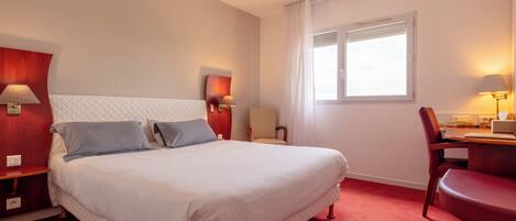 A hotel room with a large bed, a desk, a chair, and a TV.