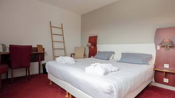 A hotel room with a large bed, a desk with a chair, a wooden ladder, and a nightstand with a lamp.