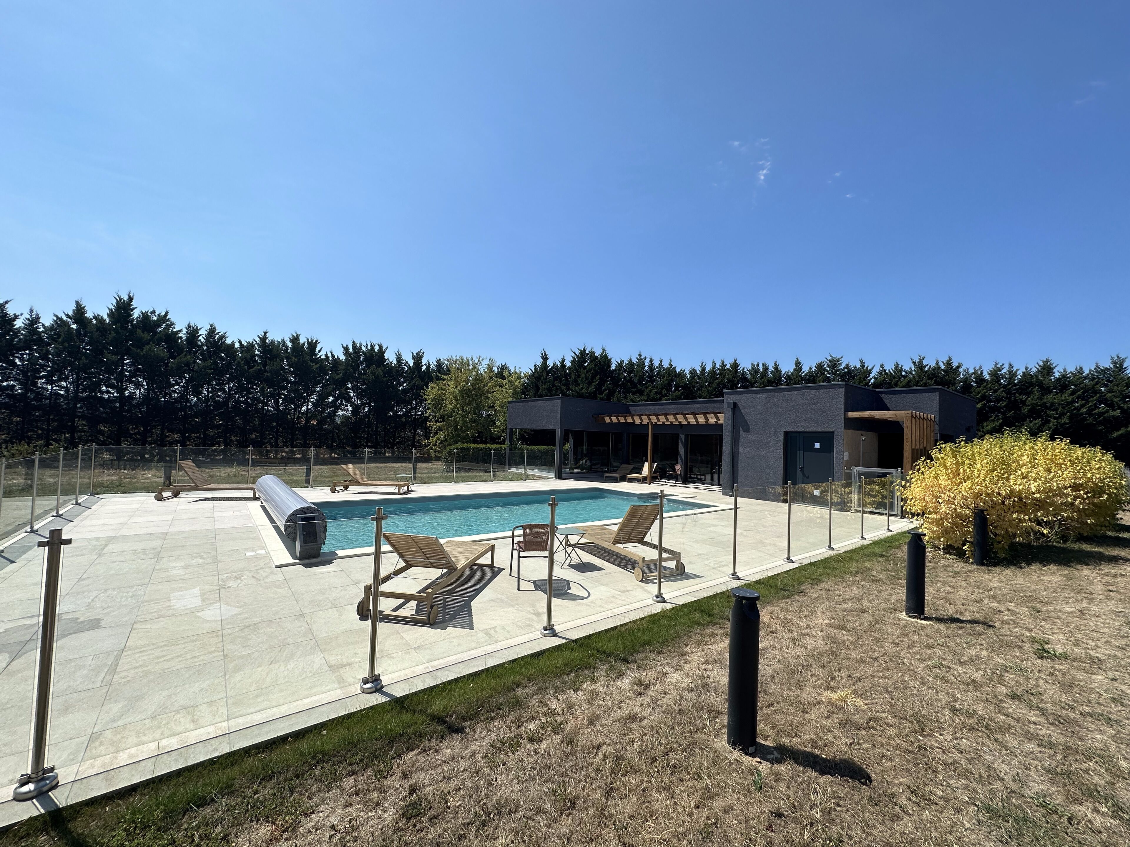 Un área de piscina moderna al aire libre con sillas de descanso y un espacio de estar techado.