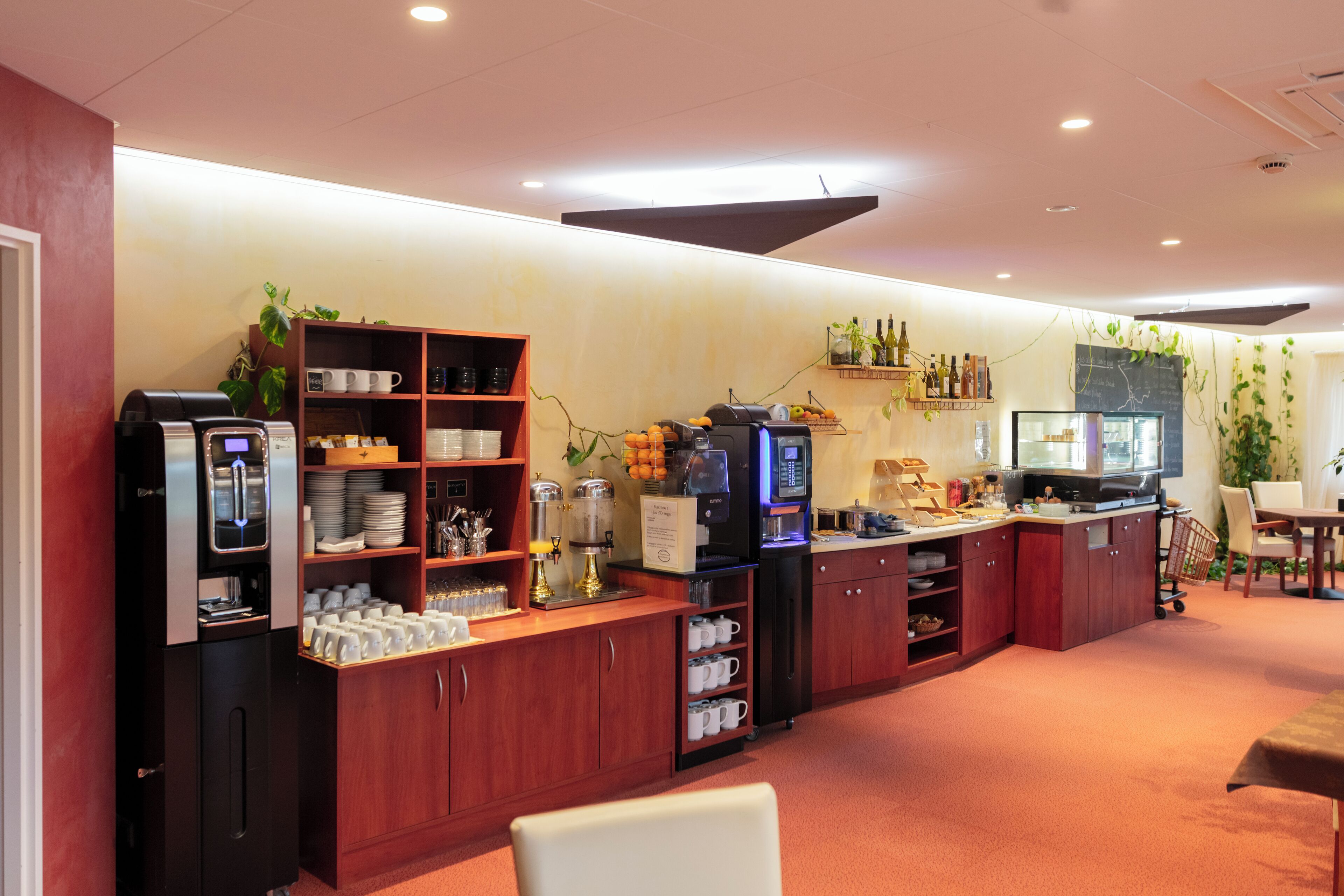 A modern kitchen area with coffee machines, a refrigerator, and a dining table with chairs.